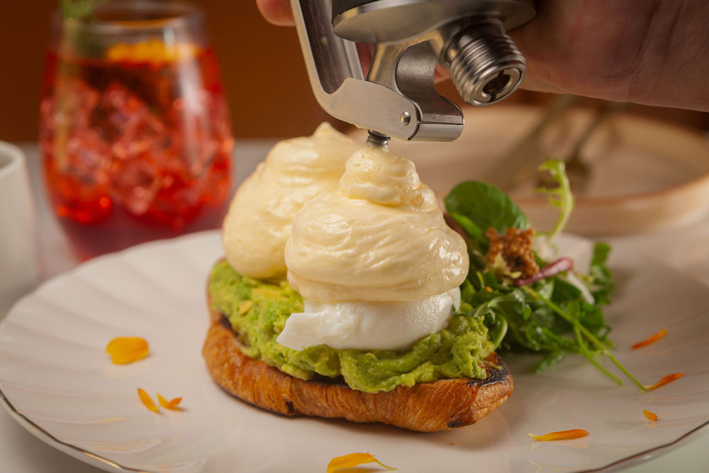 Avocado benedict with hollandaise foam being piped tableside